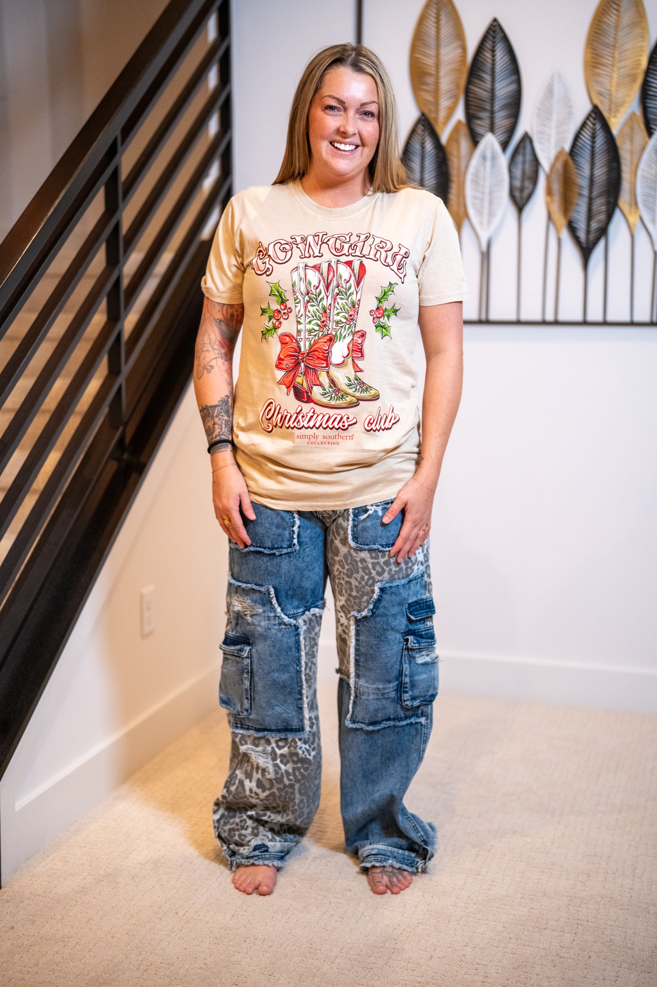 Person wearing a decorated t-shirt and patchwork jeans standing in a room with decorative wall art.