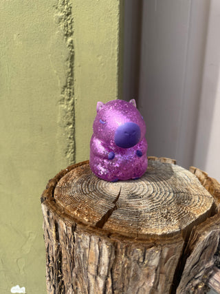Purple object with a blue sphere on a wooden log against a green wall.