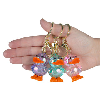 Three colorful duck-shaped keychains held in a hand against a white background