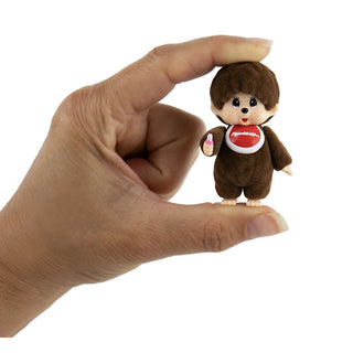 Hand holding tiny brown Monchhichi toy figure against white background