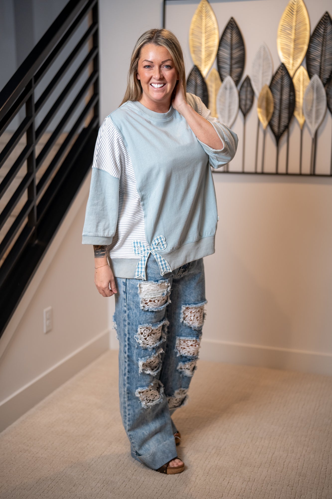 Woman wearing a light blue sweater and ripped jeans indoors.