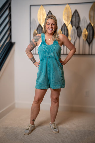 Woman wearing a teal romper standing in a room with decorative wall art.