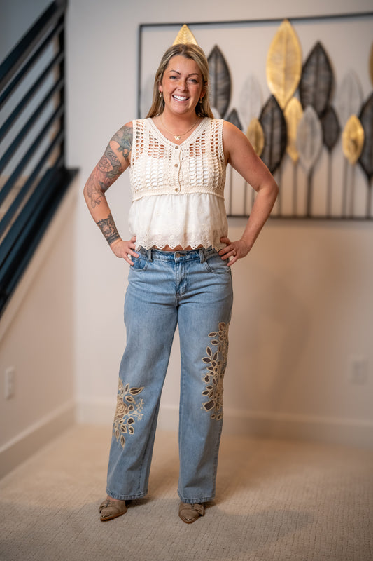 Woman wearing a sleeveless top and light jeans with intricate cutout lace detail 