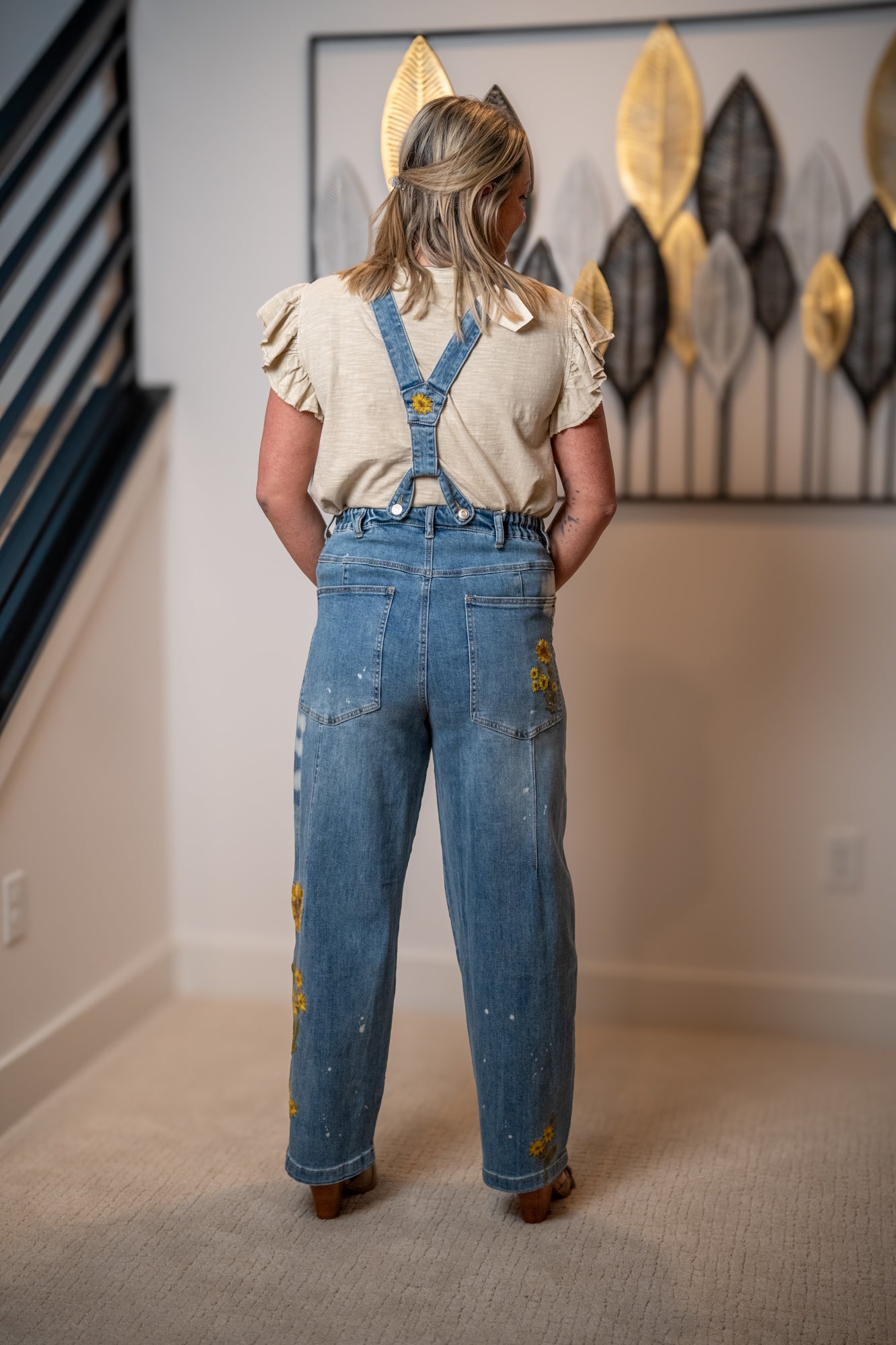 Back view of Oli and Hali denim overalls with sunflower embroidery and adjustable suspenders