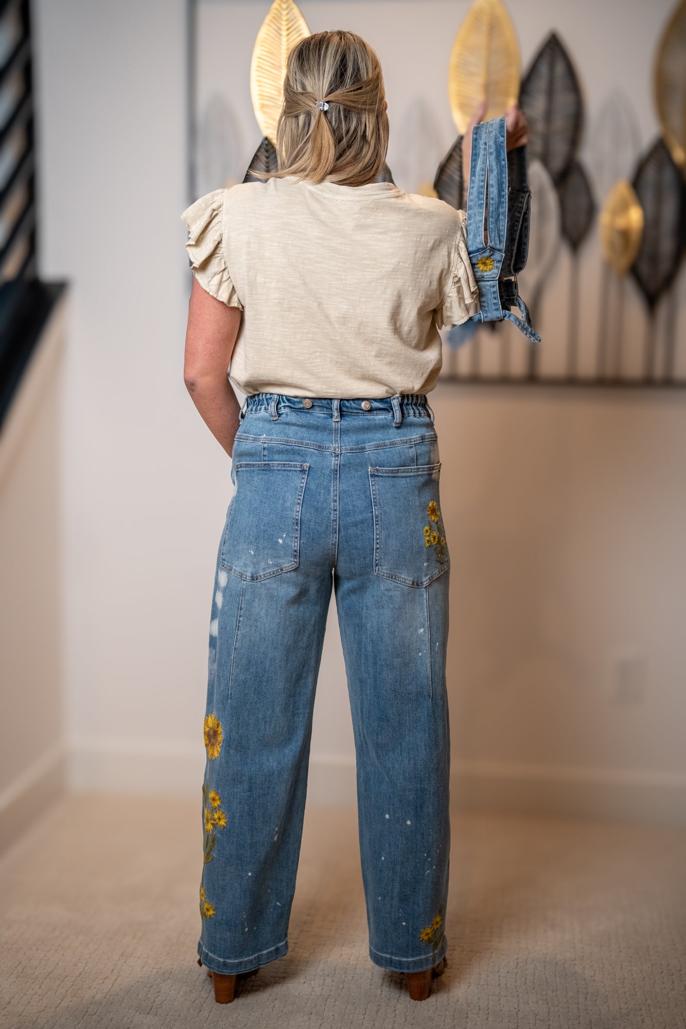 Back view of sunflower embroidered wide leg jeans with high rise fit and detachable straps