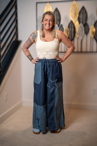 Woman wearing a white top and blue patchwork pants in a room with decorative wall art.