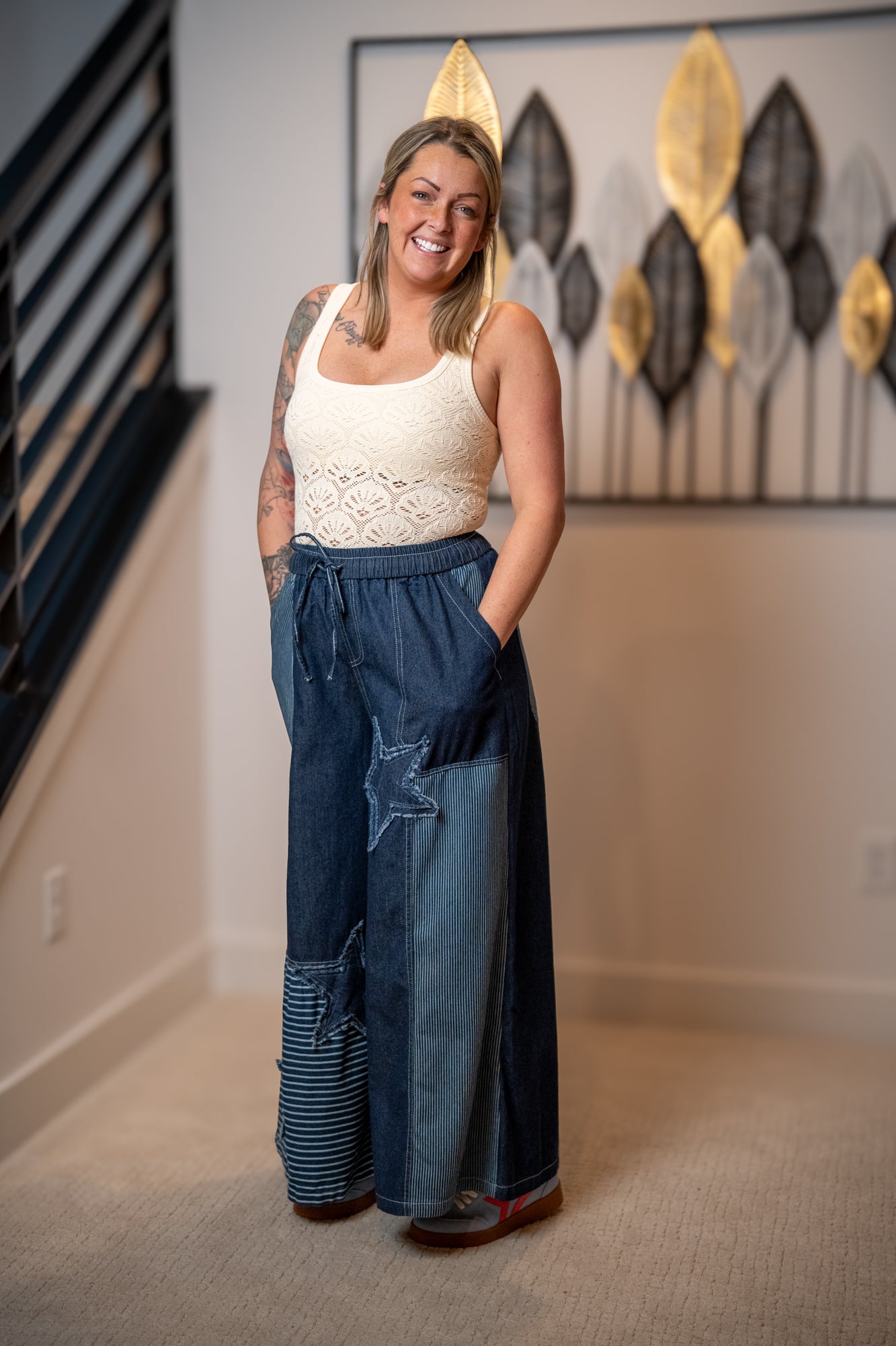 Woman wearing a white top and blue denim pants standing in a room with decorative wall art.