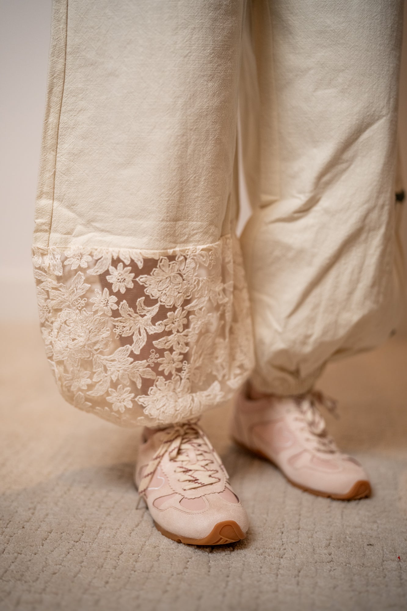 Close-up of white lace-trimmed pants and matching shoes on a neutral background