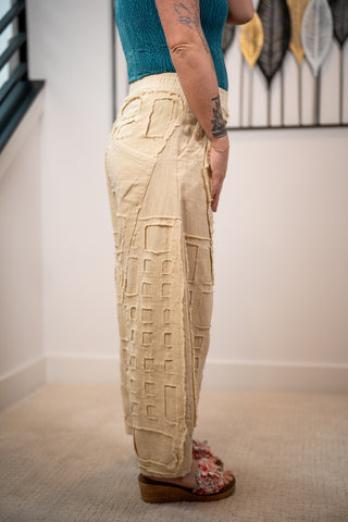 Person wearing beige textured pants with a white wall and decorative item in the background