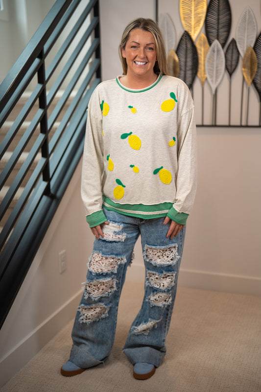 Woman wearing a sweater with lemon patterns and ripped jeans indoors.