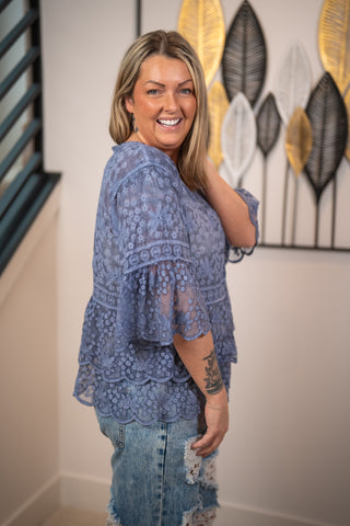 Woman wearing a blue lace top and jeans standing in front of a wall with abstract art.