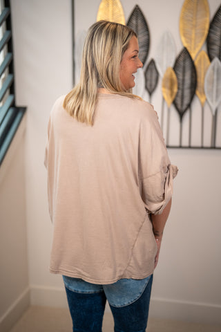 Woman wearing a beige long-sleeve top and blue jeans standing in a room with decorative wall art.