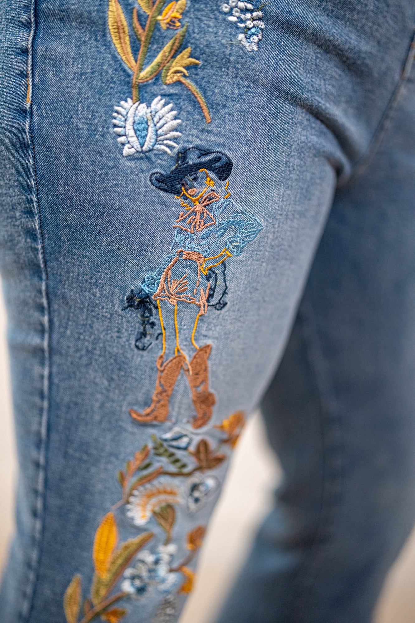 Embroidered design on denim fabric featuring a cowgirl and floral elements.