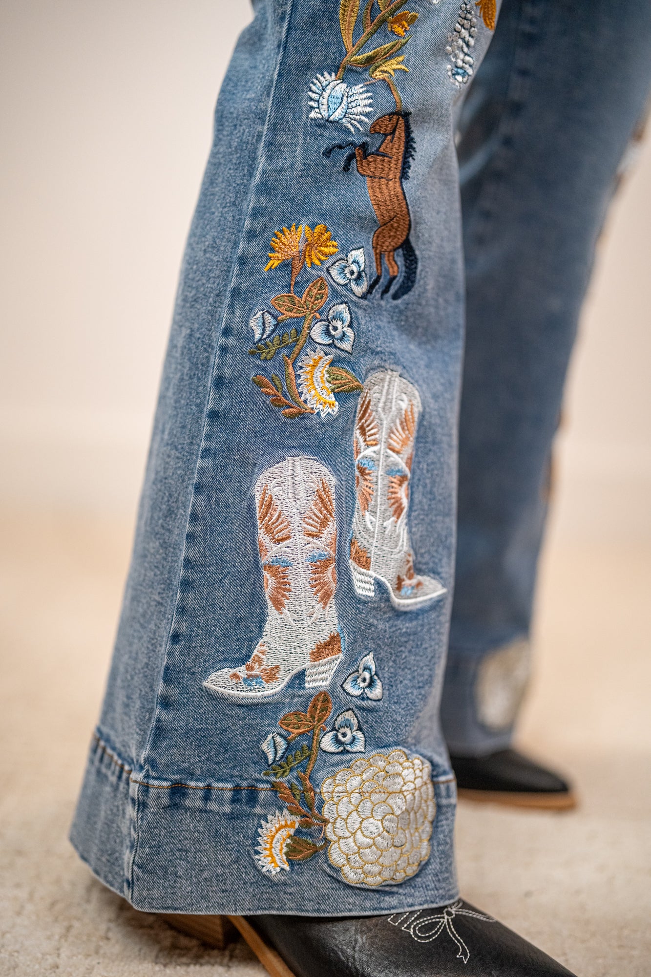 Close-up of embroidered jeans with cowboy boots and flowers on a blurred background