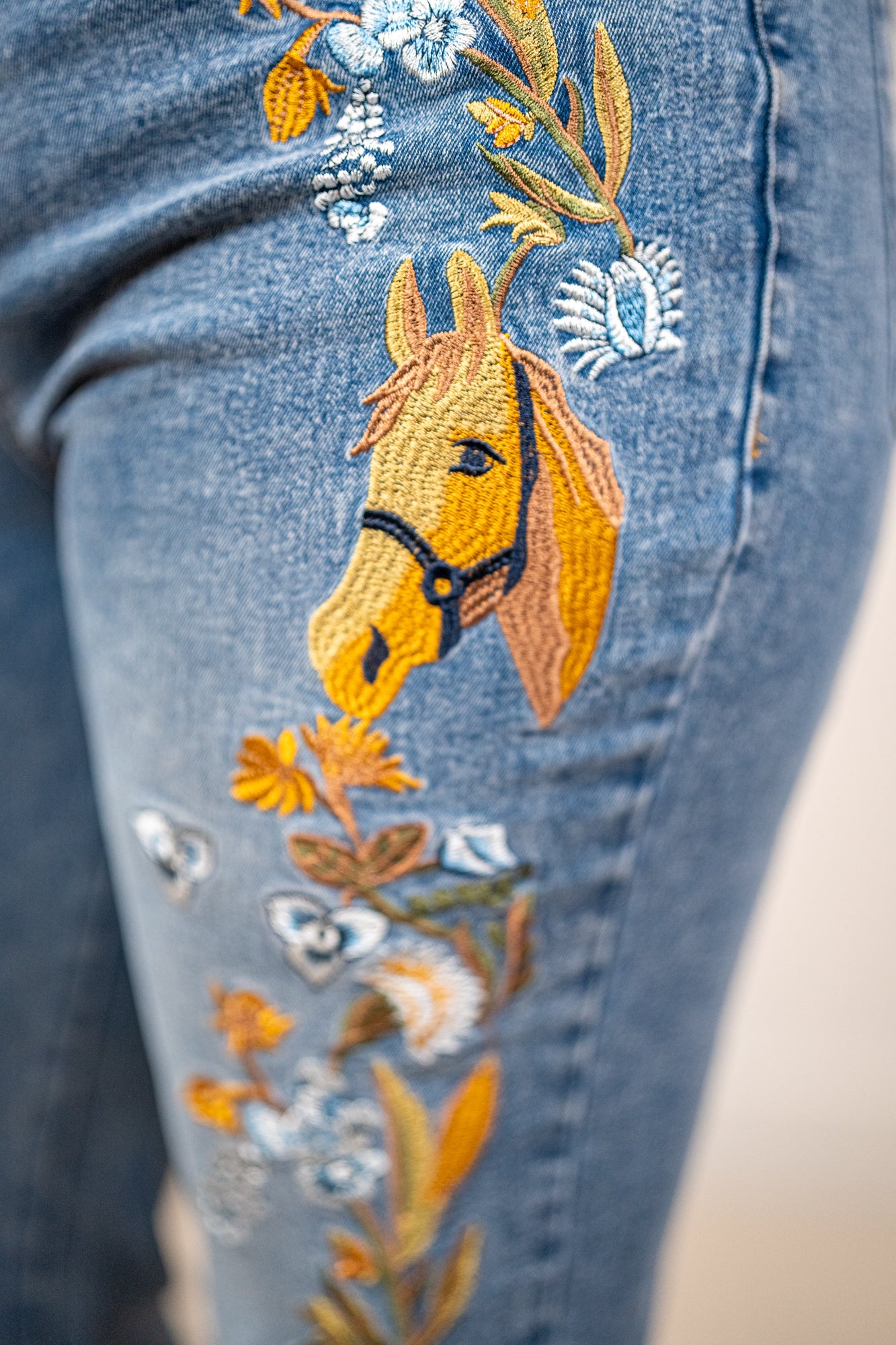 Embroidered horse design on a blue denim fabric with floral elements.