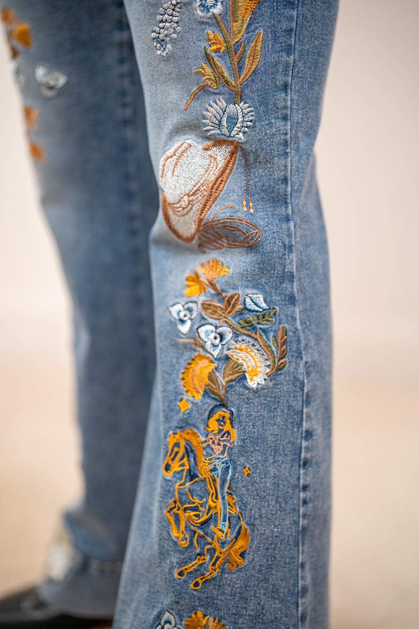 Close up of Blue B western embroidered flare jeans with floral stitching, cowboy and boot design