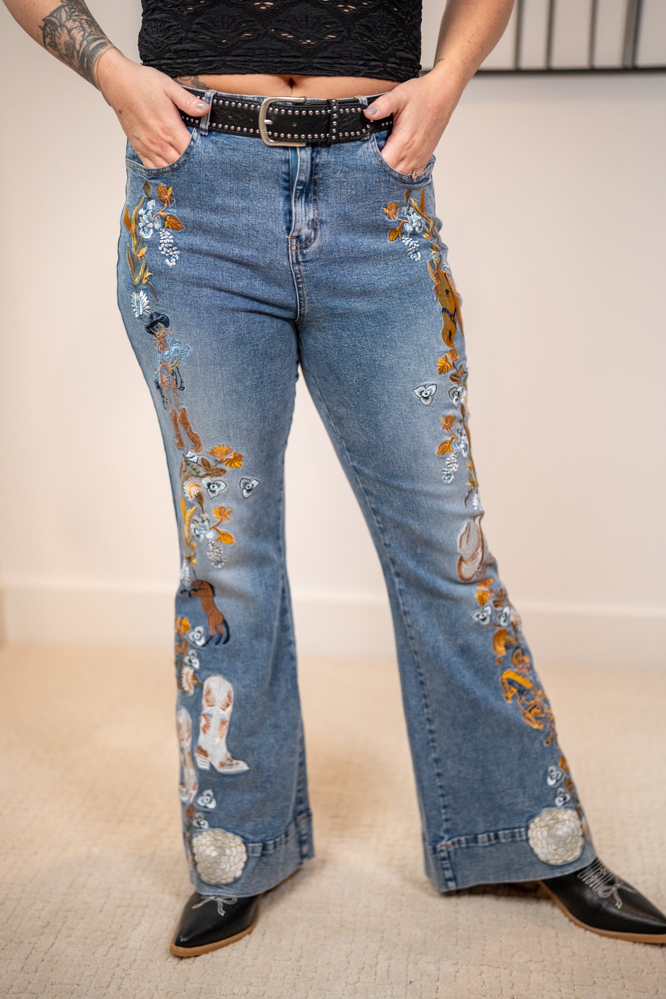 Person wearing blue jeans with western embroidery with black belt black boots and black tank