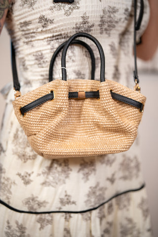 Close up of natural straw handbag with black leather handles and gold hardware