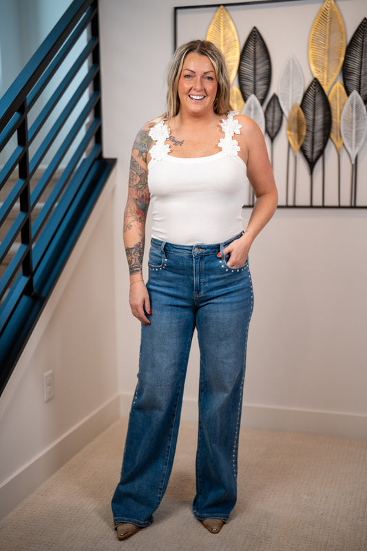 White ribbed tank top with 3D floral strap detail and fitted stretch silhouette paired with dark denim