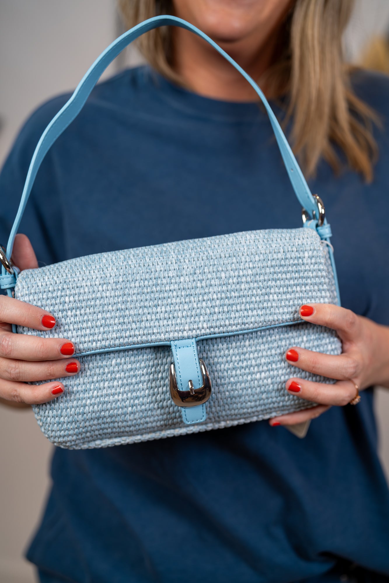 Close up of Light blue woven straw shoulder bag with silver hardware and adjustable strap
