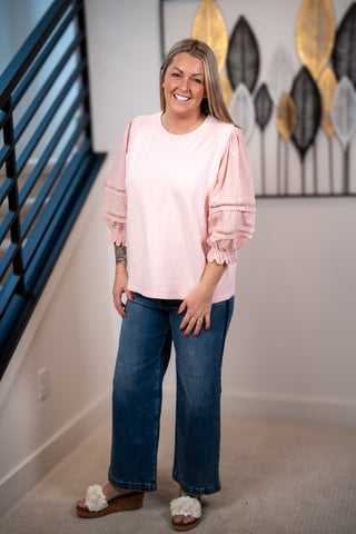 Woman wearing a pink blouse and blue jeans standing in a room with decorative wall art.