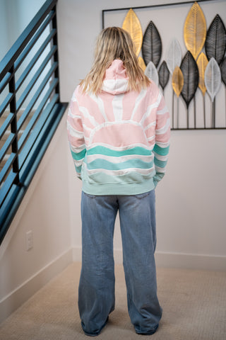 Person wearing a colorful striped sweater and blue jeans standing in a room with a decorative wall piece.