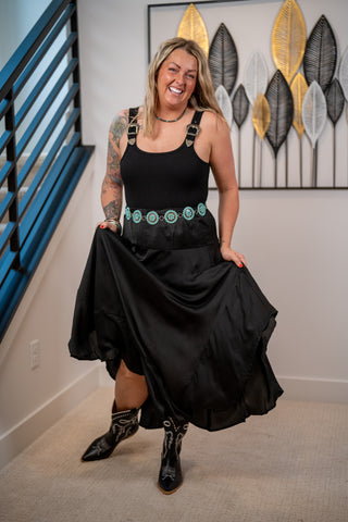 Woman in a black dress with green accents standing in a room with decorative wall art.