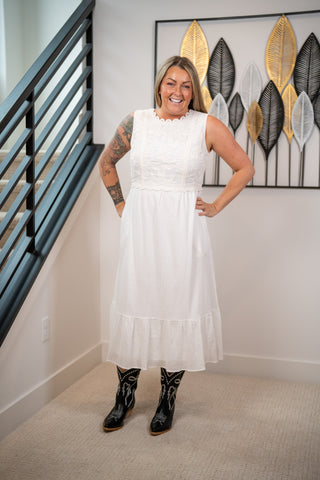 Woman in a white dress with black boots standing in a room with decorative wall art.
