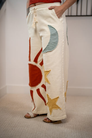 White pants with sun and star designs worn by a person indoors.