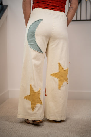 White pants with star and moon patches worn by a person indoors.