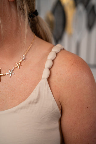 Close-up of a person wearing a beige top and gold necklace with starfish designs.