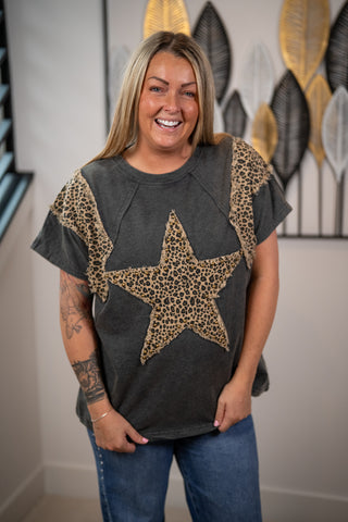 Woman wearing a dark gray t-shirt with a large star design, standing indoors.