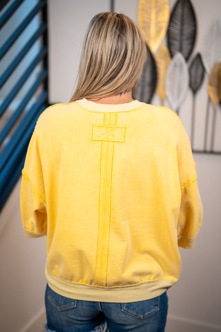 A woman viewed from behind wearing a yellow cropped sweatshirt with a unique vertical stitched detail on the back, paired with blue jeans in an indoor setting.