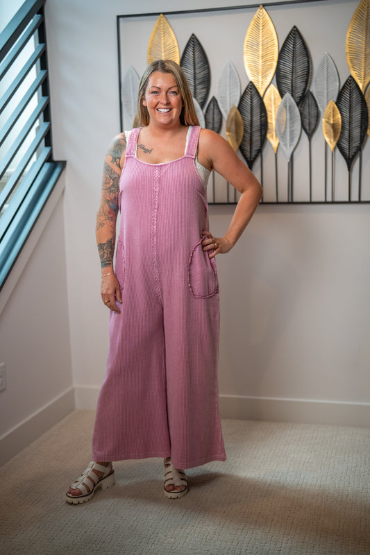 Woman wearing a pink jumpsuit standing in a room with decorative wall art.