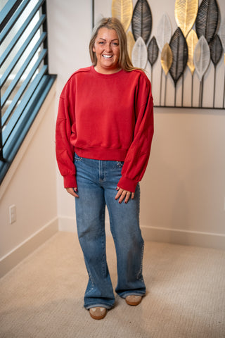 Red crew neck sweatshirt with star patch sleeves, worn with wide-leg jeans