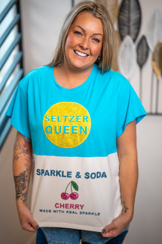 Woman wearing a blue and white t-shirt with 'Seltzer Queen' and cherry graphics by queen of sparkels.