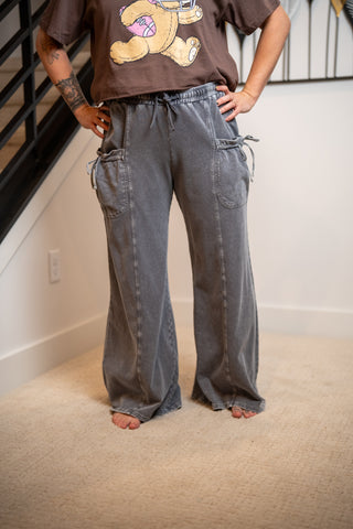 Person wearing a brown t-shirt with a graphic design and gray baggy pants in an indoor setting.