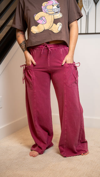 Person wearing a brown t-shirt with a teddy bear graphic and magenta pants indoors.