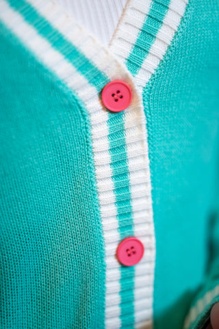 Teal knit cardigan with white ribbed button band and pink buttons