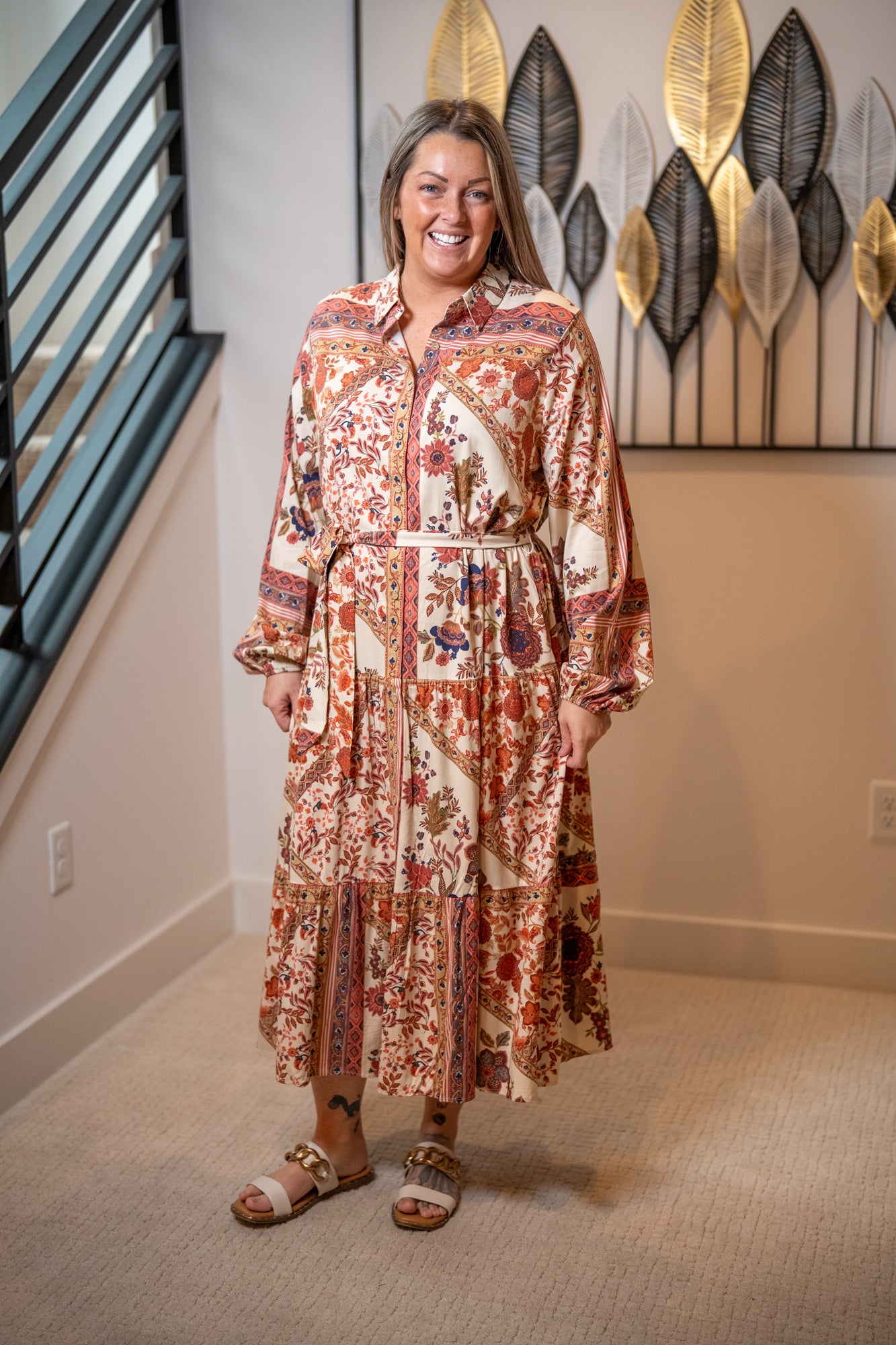 Woman wearing a patterned dress standing in a room with decorative wall art.