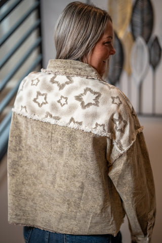 Woman wearing a beige jacket with star patterns on the back, standing indoors.