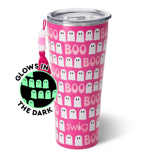 A pink tumbler with a pattern of white ghosts that says 'BOO' and 'SWIG' on it, alongside a silicone coaster with a string.