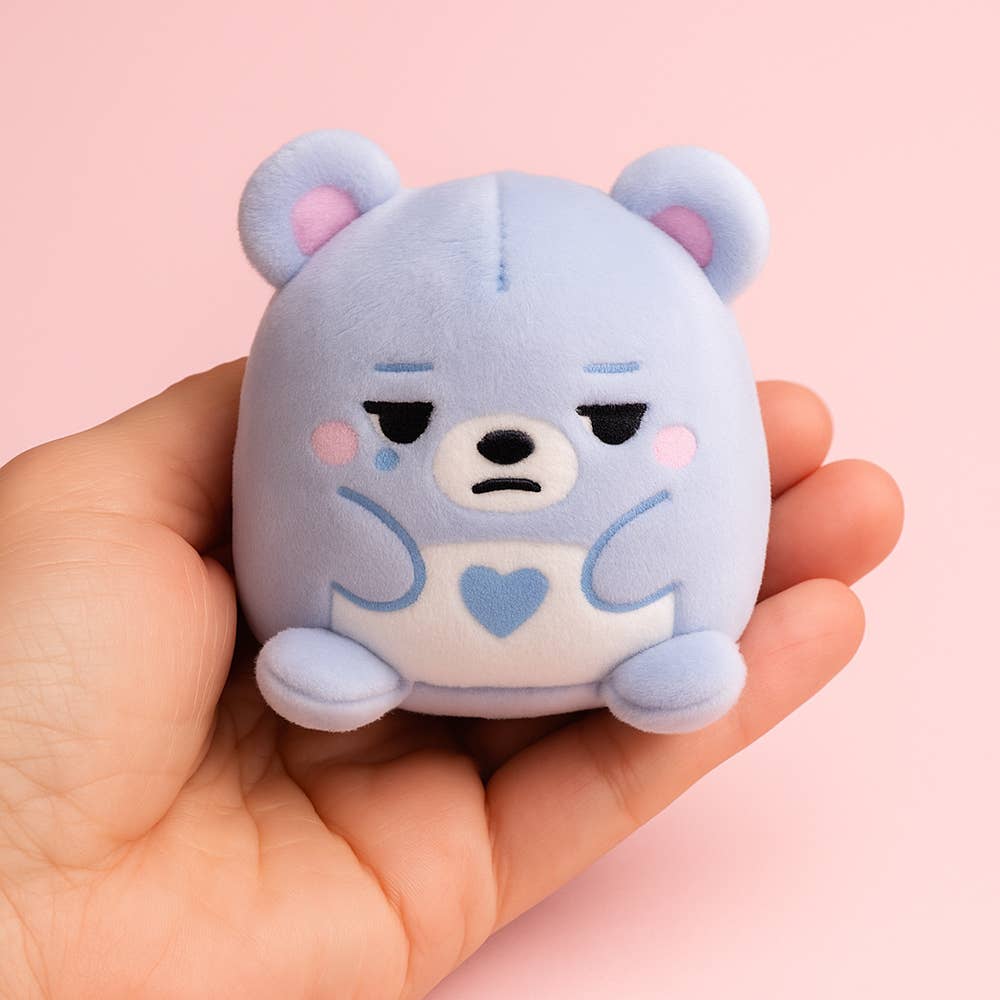Cute blue plush toy held in a hand against a pink background