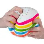 Hands squeezing a rainbow-layered cake squishy toy with white frosting and sprinkles