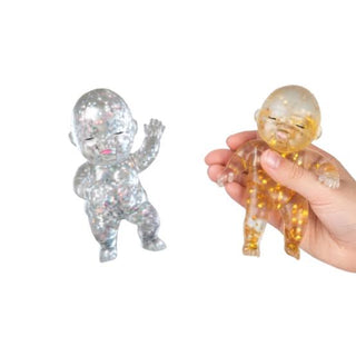 Two glitter-filled squishy baby figures in silver and gold, one held in hand