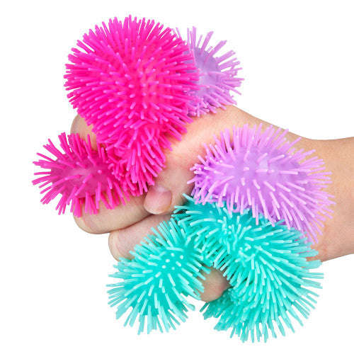 Hands holding colorful spiky sensory balls in pink, purple, and teal colors